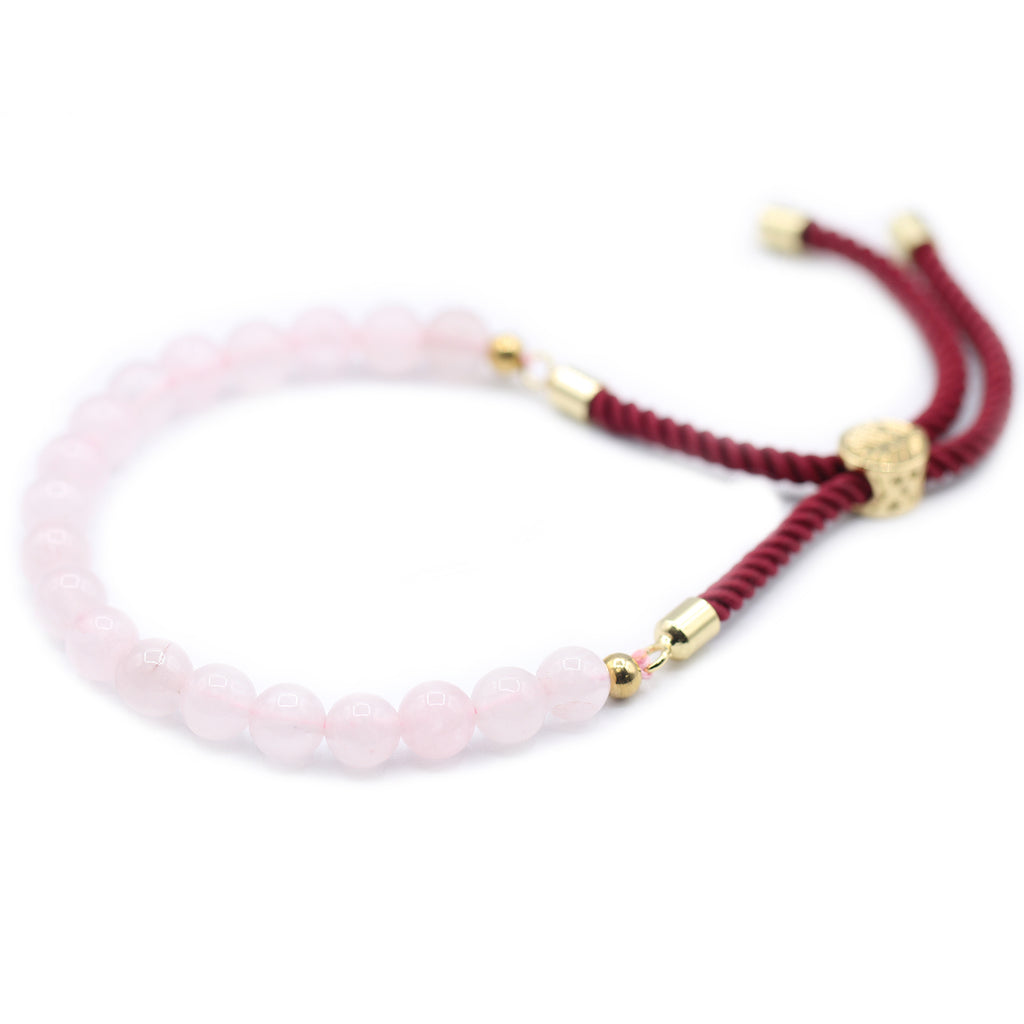A rose quartz beaded bracelet on a red strong and golden fittings, on a white surface 