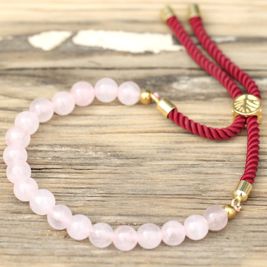 A rose quartz beaded bracelet on a red strong and golden fittings, on a wooden surface 