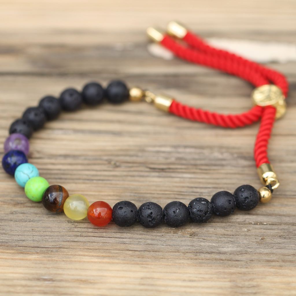 A 18K gold plated red string bracelet with lava stone chakra beads on a wooden surface.