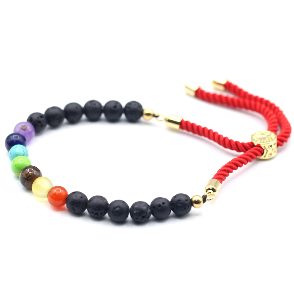 A 18K gold plated red string bracelet with lava stone chakra beads on a white surface.