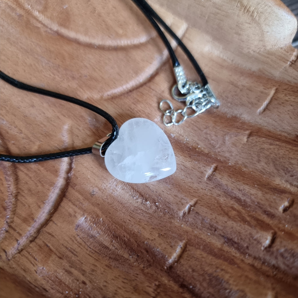 A white crystal heart on a black cord necklace displayed on a pair of wooden hands