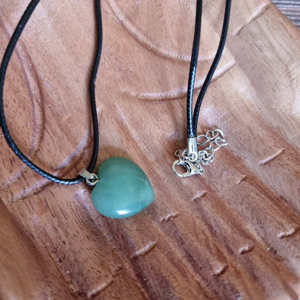 A green crystal heart on a black cord necklace displayed on a pair of wooden hands