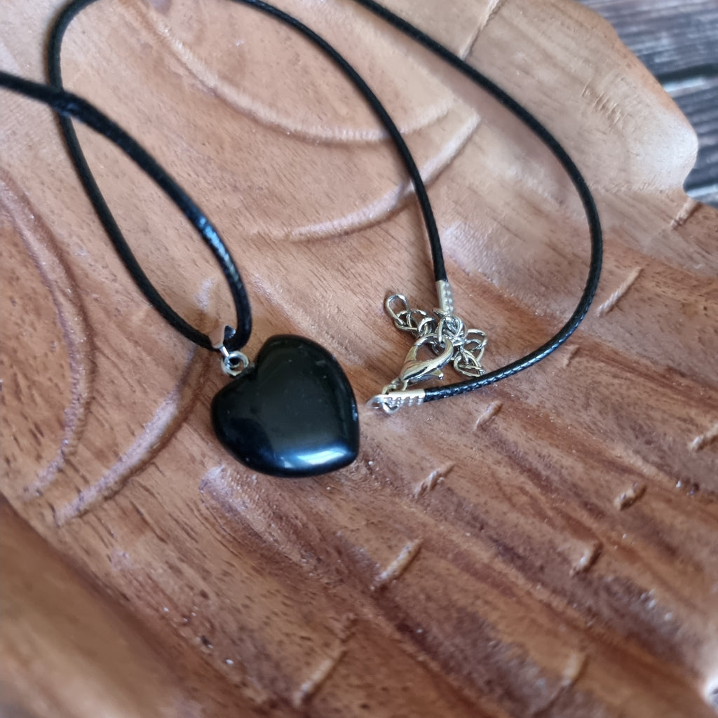 A black crystal heart on a black cord necklace displayed on a pair of wooden hands