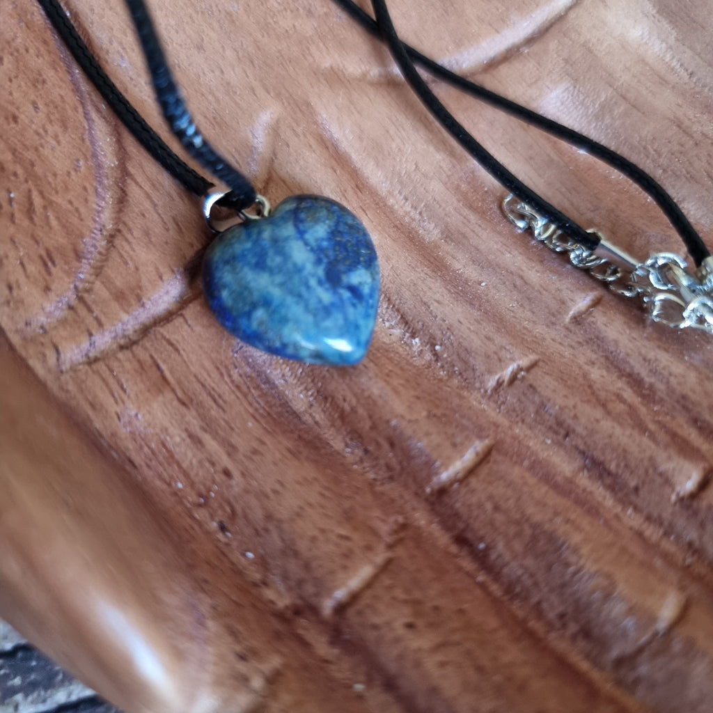 A blue crystal heart on a black cord necklace displayed on a pair of wooden hands