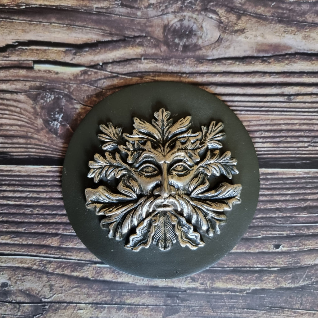 A bronze-effect green man incense holder made of resin, displayed on a wooden surface 