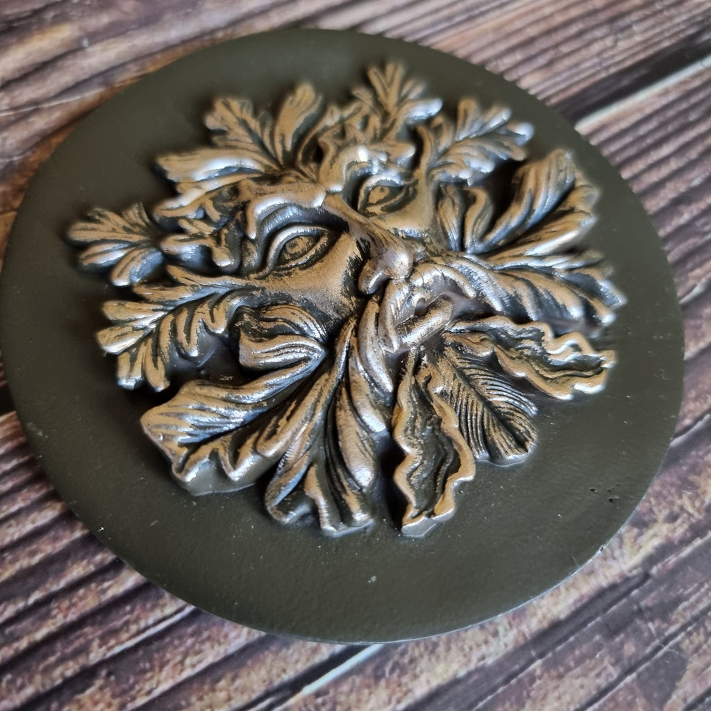 A bronze-effect green man incense holder made of resin, displayed on a wooden surface 