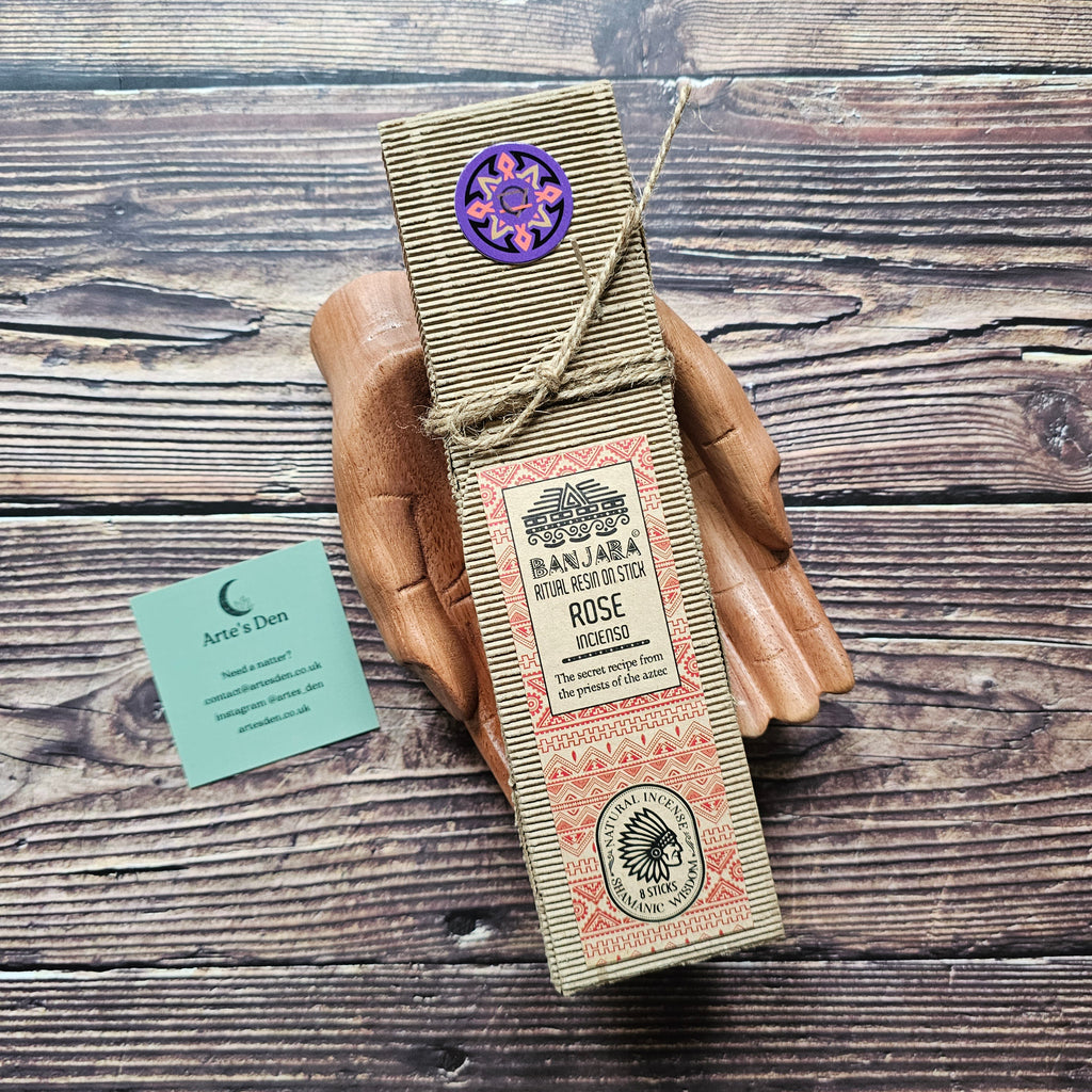 Beige packaged ritual incense sticks laid on a pair of wooden hands on a wooden backdrop. 