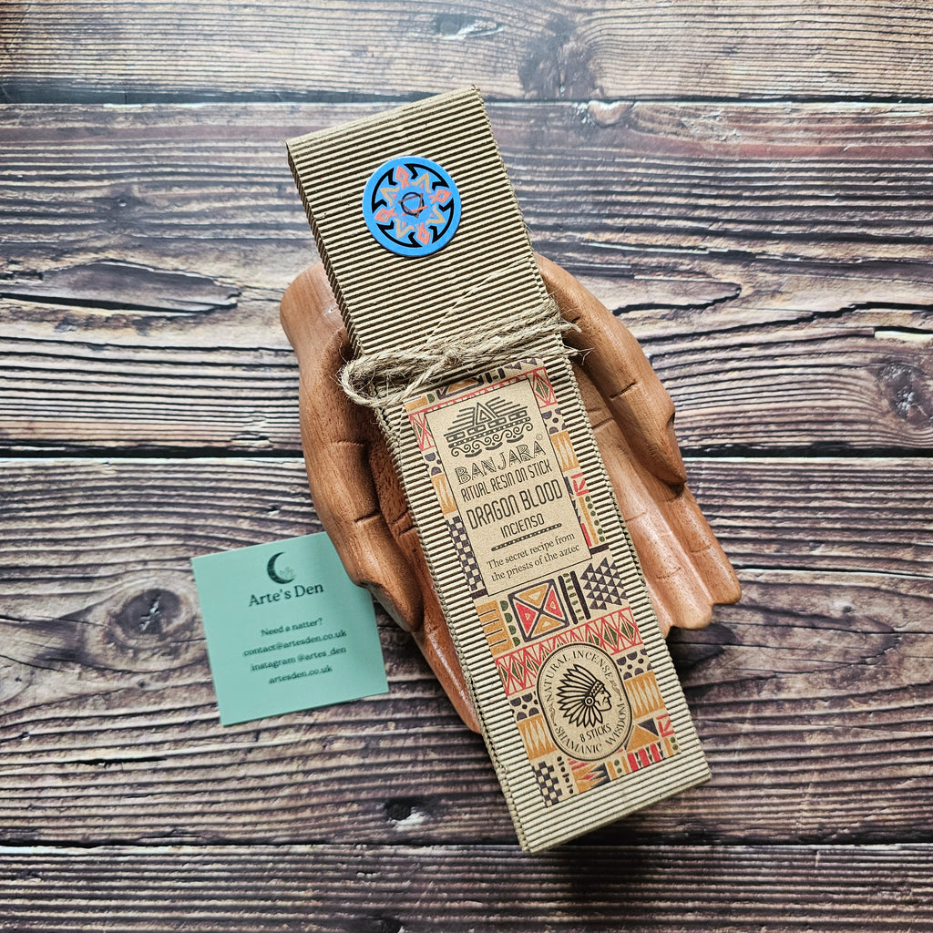 Beige packaged ritual incense sticks laid on a pair of wooden hands on a wooden backdrop. 