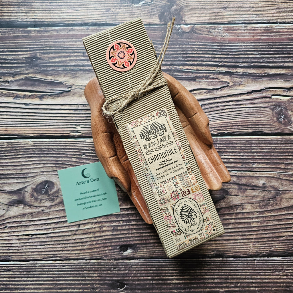 Beige packaged ritual incense sticks tied with string, laid on a pair of wooden hands. 