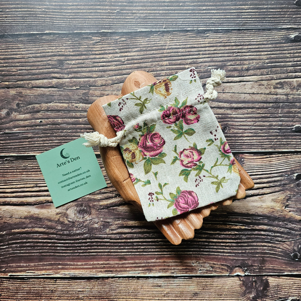 A floral bag displayed on a pair of wooden hands, with a business card that reads 'Arte's Den'.