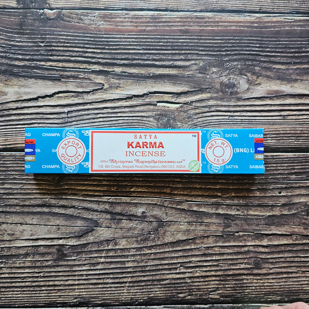 A pack of Satya incense sticks with the label 'KARMA' displayed on the packaging. Laid on a wooden background. 