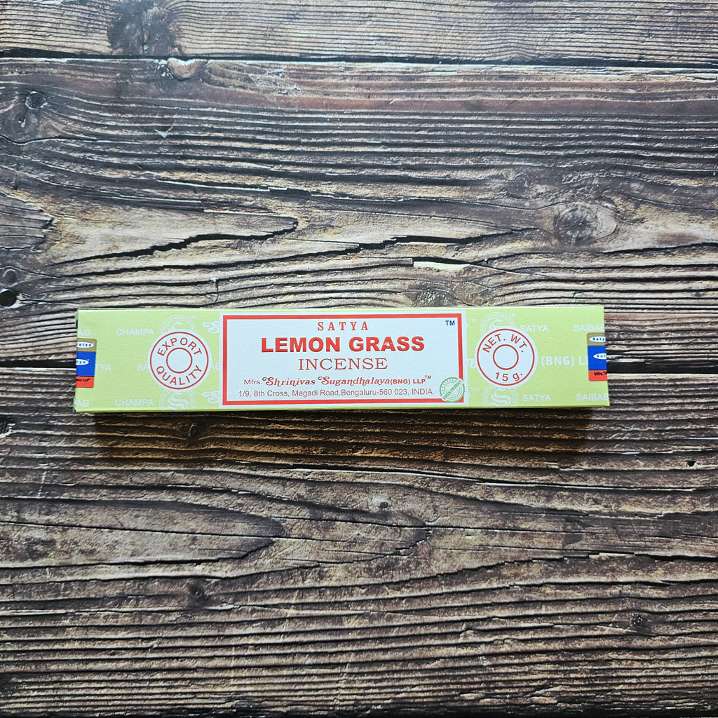A pack of Satya incense sticks with the label 'LEMON GRASS' displayed on the packaging. Laid on a wooden background. 