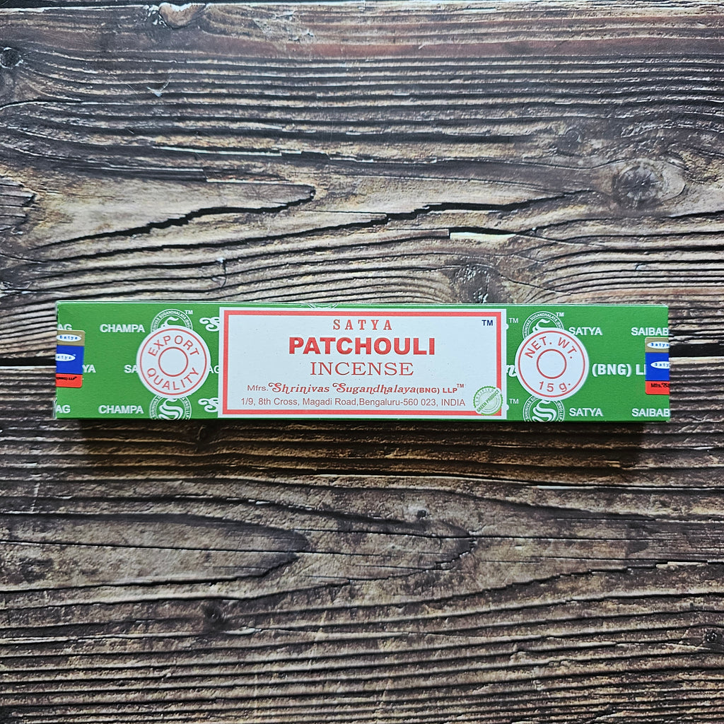 A pack of Satya incense sticks with the label 'PATCHOULI' displayed on the packaging. Laid on a wooden background. 
