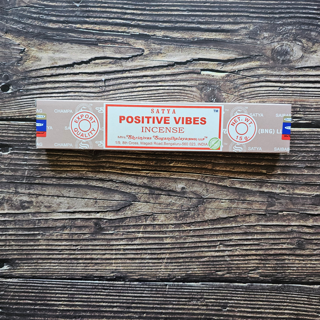 A pack of Satya incense sticks with the label 'POSITIVE VIBES' displayed on the packaging. Laid on a wooden background. 