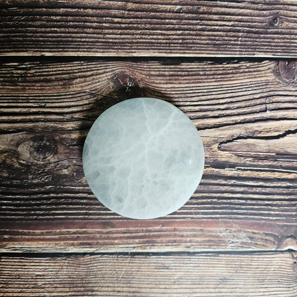 A round selenite charging plate, placed on a wooden surface.