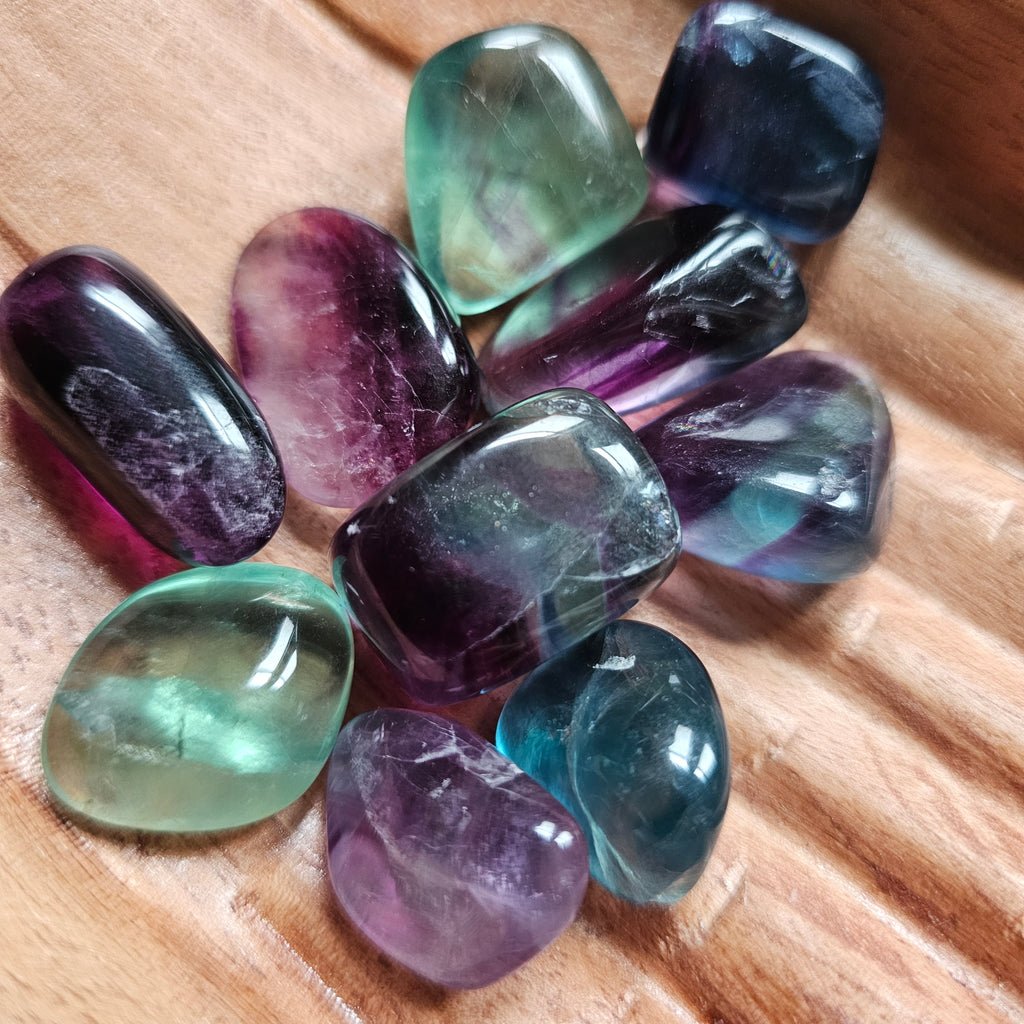 A collection of rainbow fluorite crystals in various colours including blue, green and purple, displayed in a wooden hand-shaped bowl.