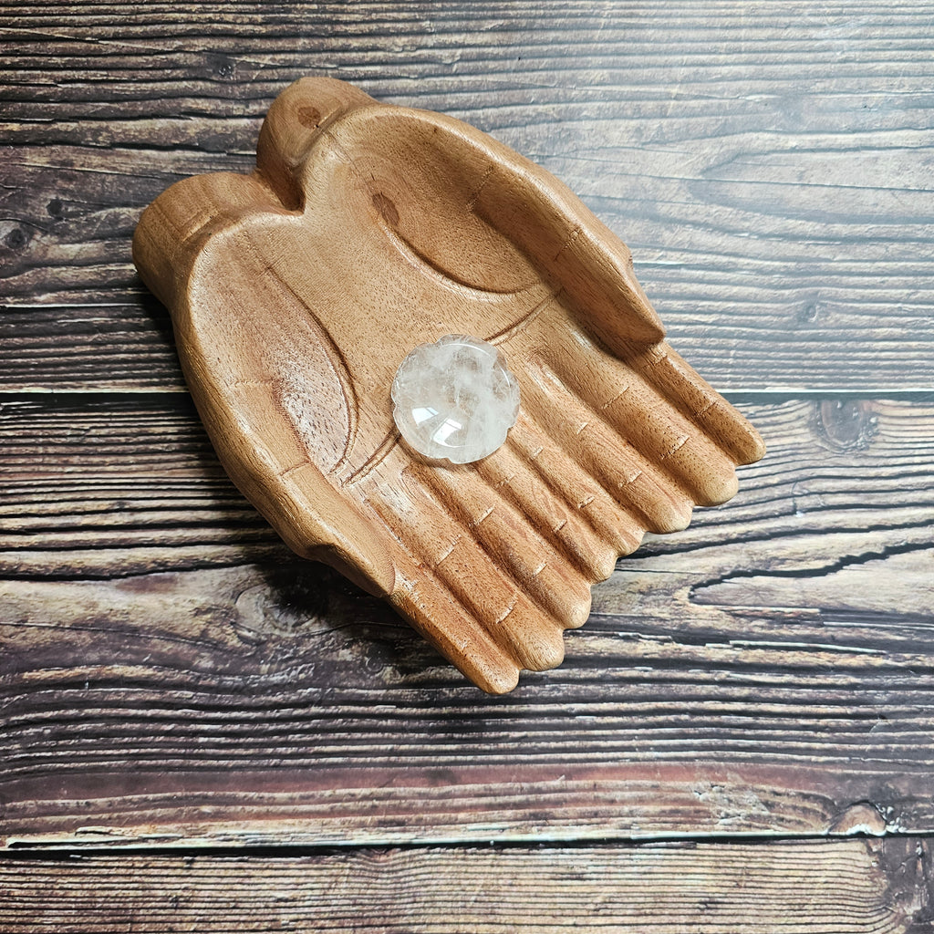 A flower shaped, clear quartz thumbstone laid on a pair of wooden hands