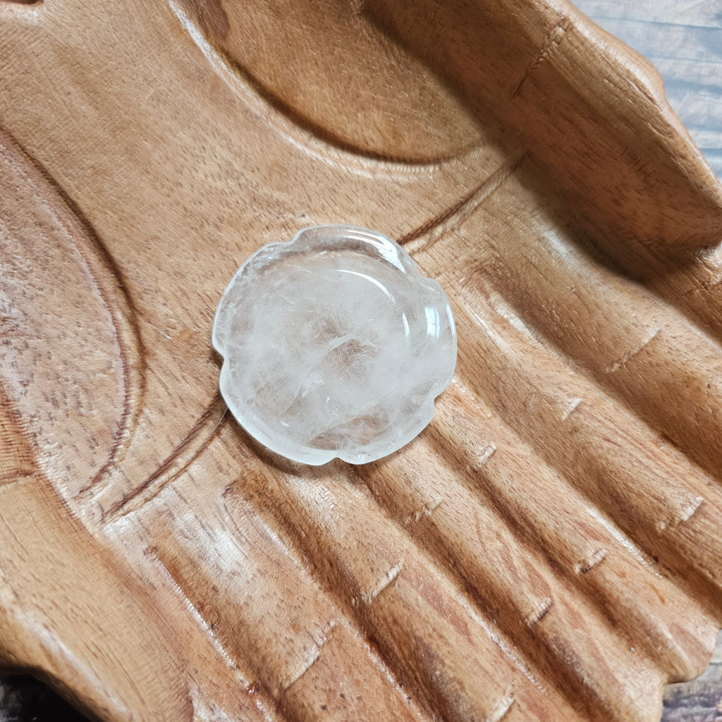 A flower shaped, clear quartz thumbstone laid on a pair of wooden hands