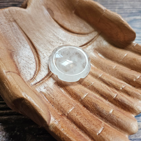 A flower shaped, clear quartz thumbstone laid on a pair of wooden hands