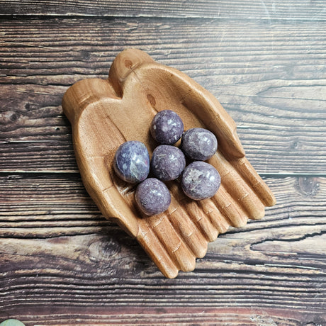 A collection of Lepidolite spheres, displayed in a wooden hand-shaped dish on a wooden background.