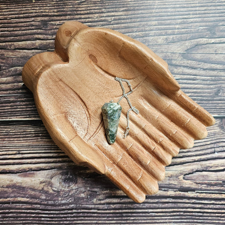 A moss agate crystal pendulum, displayed on a wooden surface.