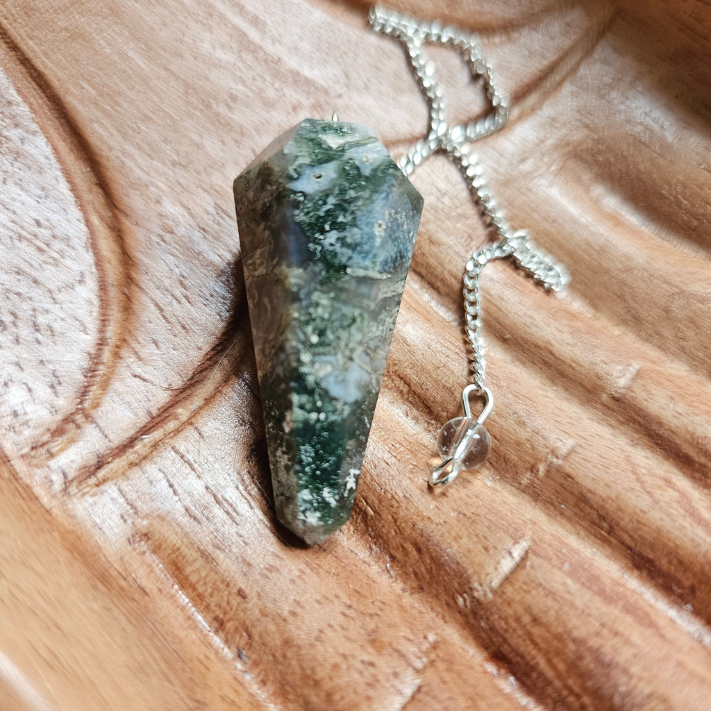 A moss agate crystal pendulum, displayed on a wooden surface.