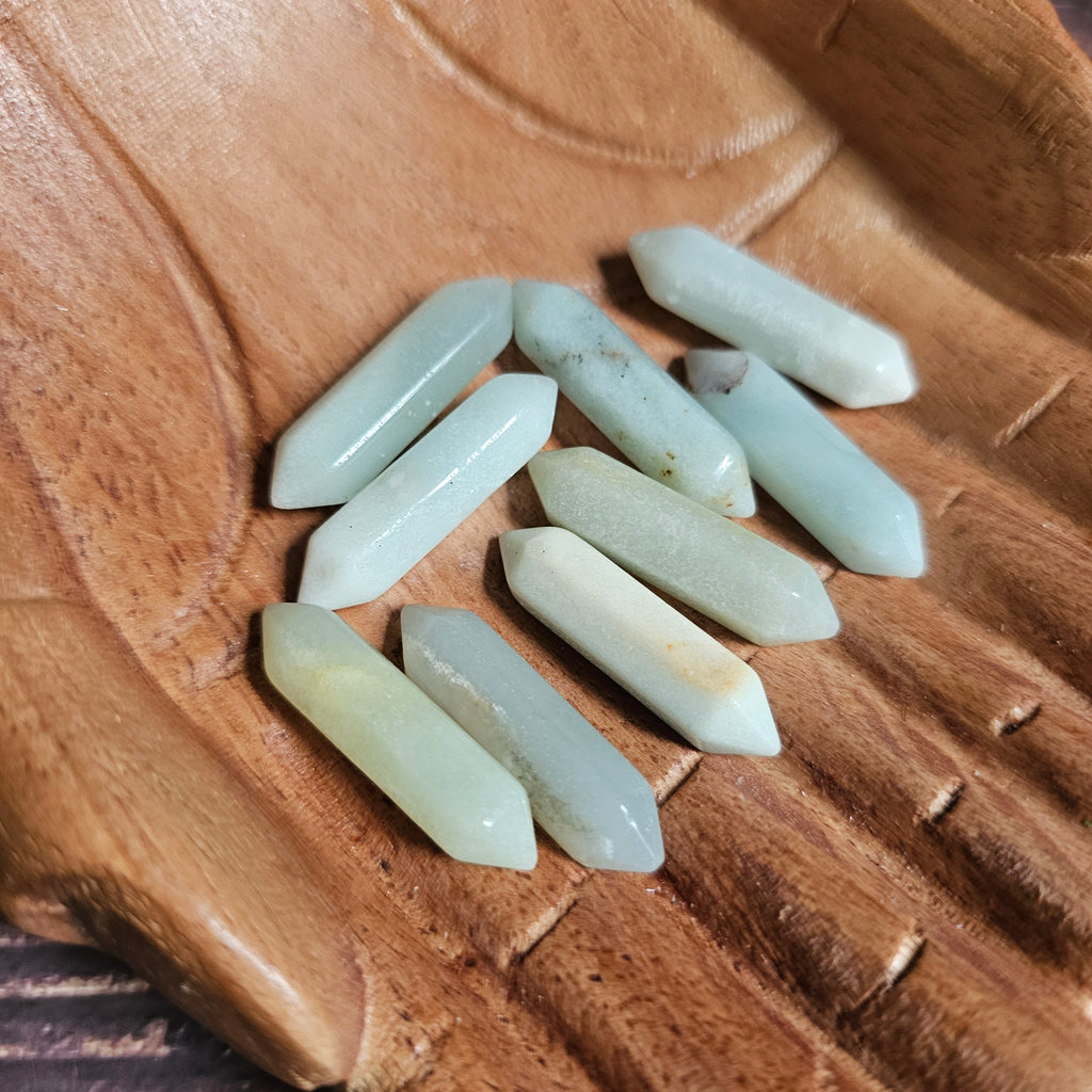 Small light green double pointed crystals held in wooden carved hands