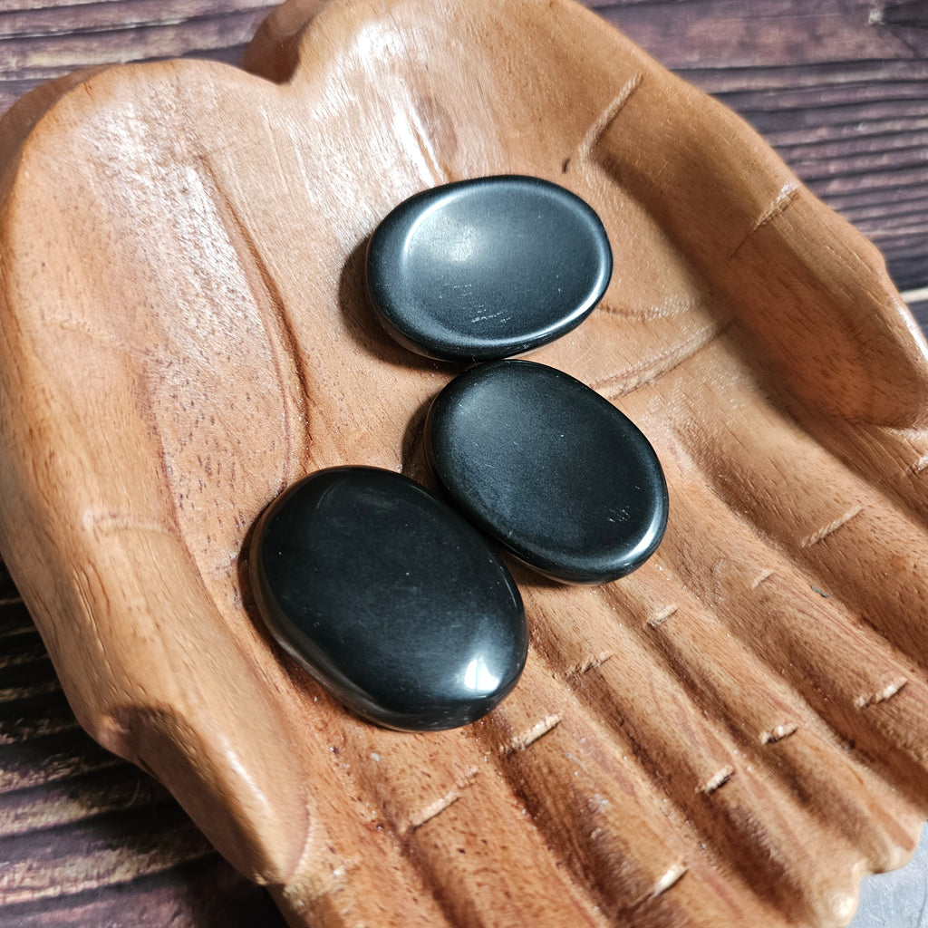 Three black polished crystal thumbstones resting on a wooden surface
