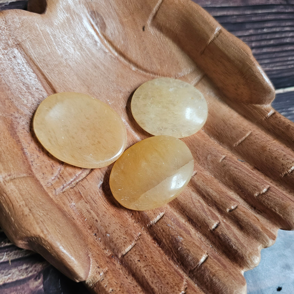 Three yellow polished crystal thumbstones resting on a wooden surface
