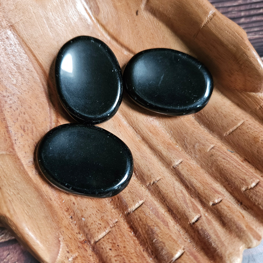 Three black polished crystal thumbstones resting on a wooden surface