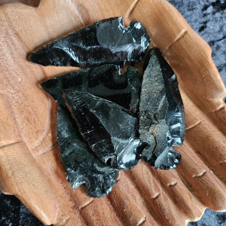 A collection of black obsidian arrow heads displayed in a pair of wooden hands