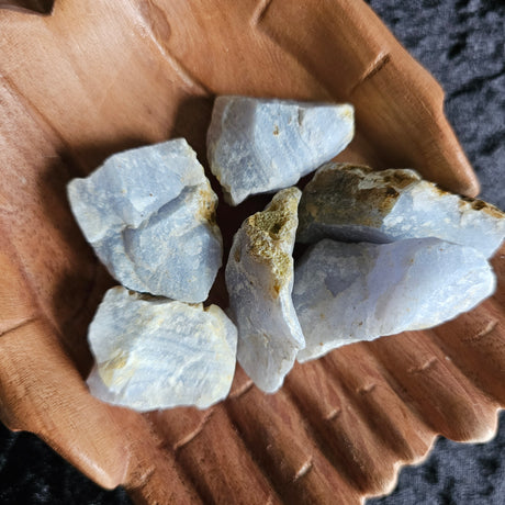 A collection of pale blue lace agate rough crystals placed on a wooden, hand-shaped dish.