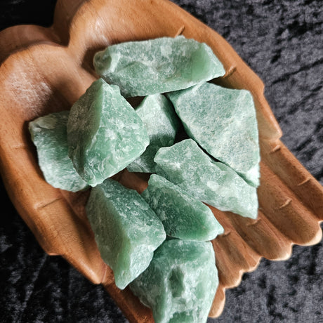 A collection of green aventurine rough stones displayed on a pair of wooden hands