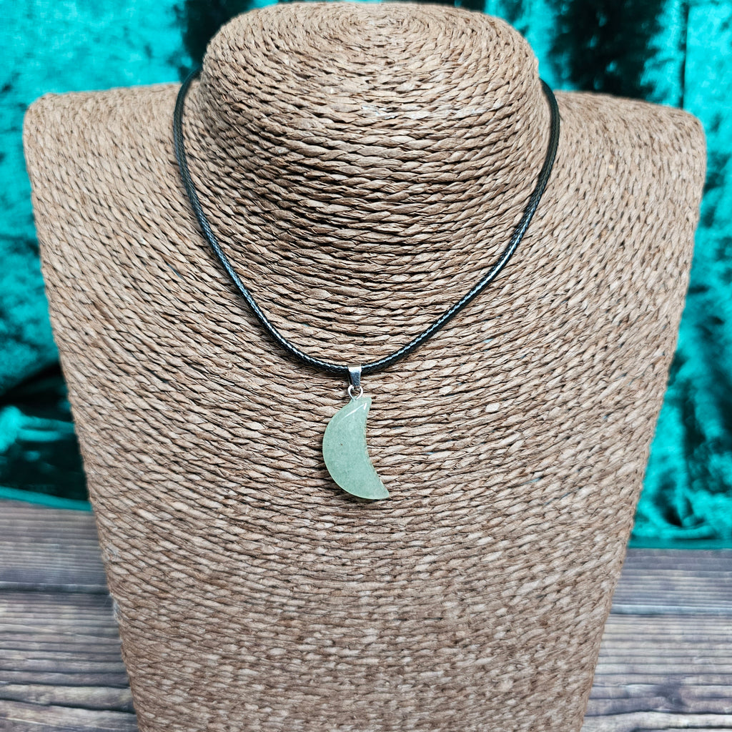 A crescent moon shaped crystal pendant on a black cord displayed on a mannequin 