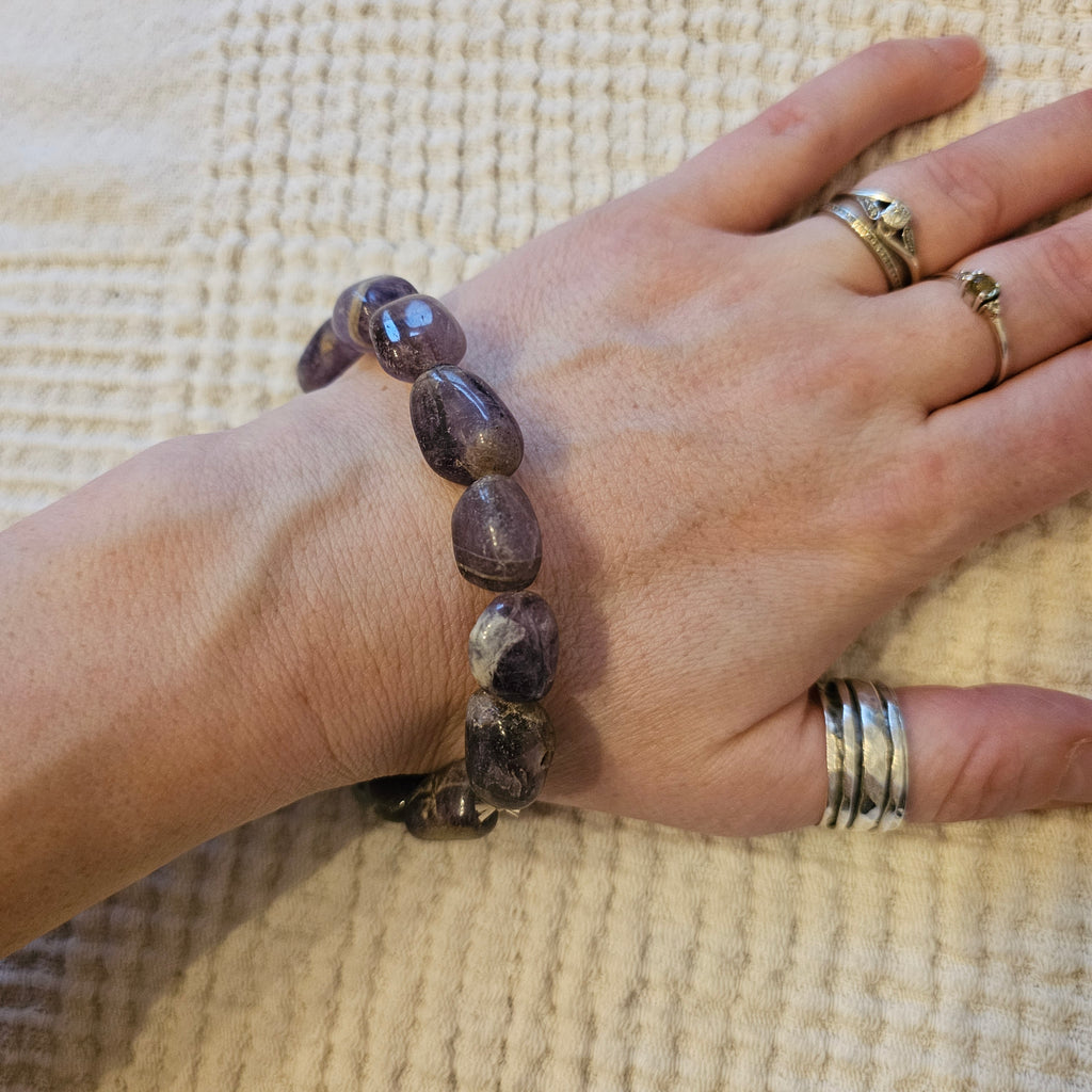A tumbled crystal bracelet in shades of purple being worn by someone. 