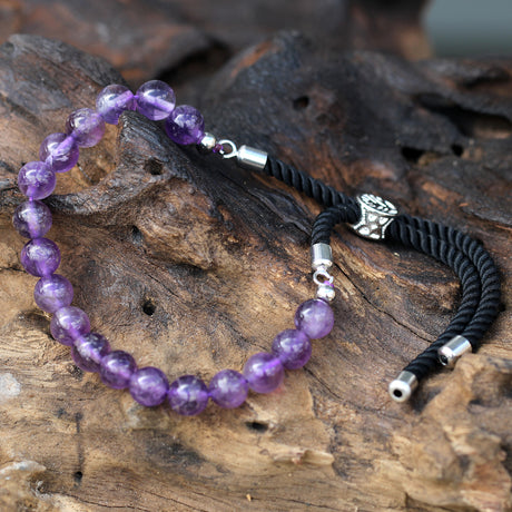 A silver-plated bracelet with black string detailing and Amethyst beads, displayed on a wooden surface.