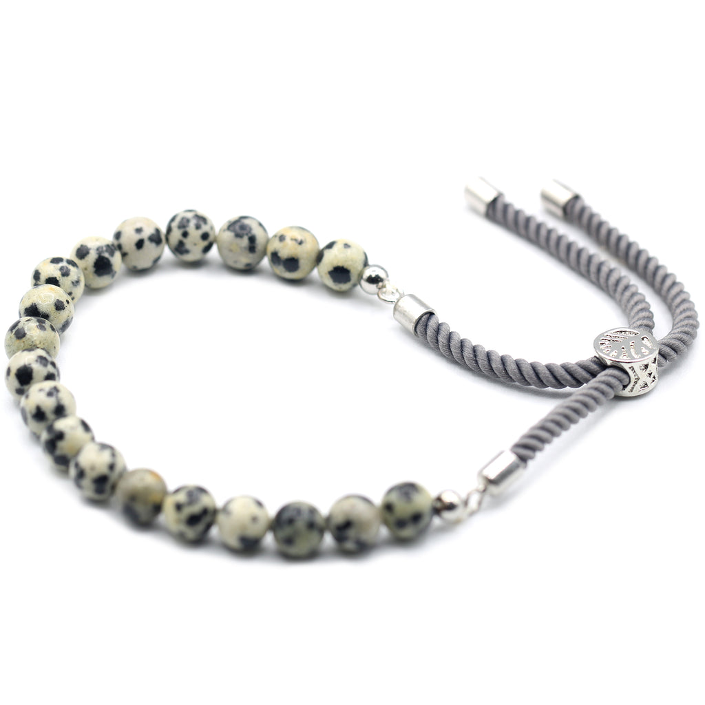 A white and black "dalmation" beaded bracelet with silver cord laid on a white surface. 