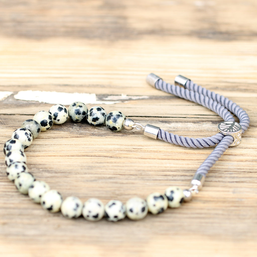 A white and black "dalmation" beaded bracelet with silver cord laid on a wooden surface. 