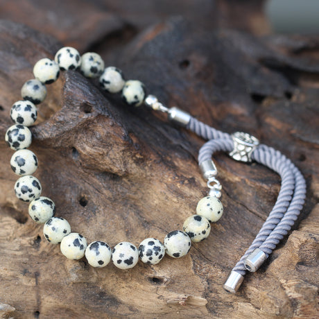 A white and black "dalmation" beaded bracelet with silver cord laid on a wooden surface. 