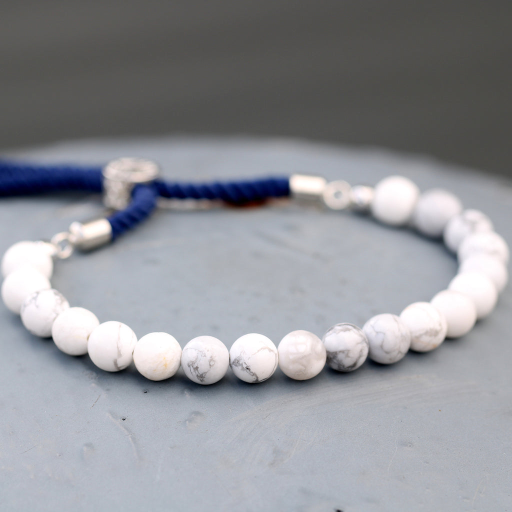 A silver-plated bracelet with navy string detailing and white howlite beads, displayed on a grey surface.