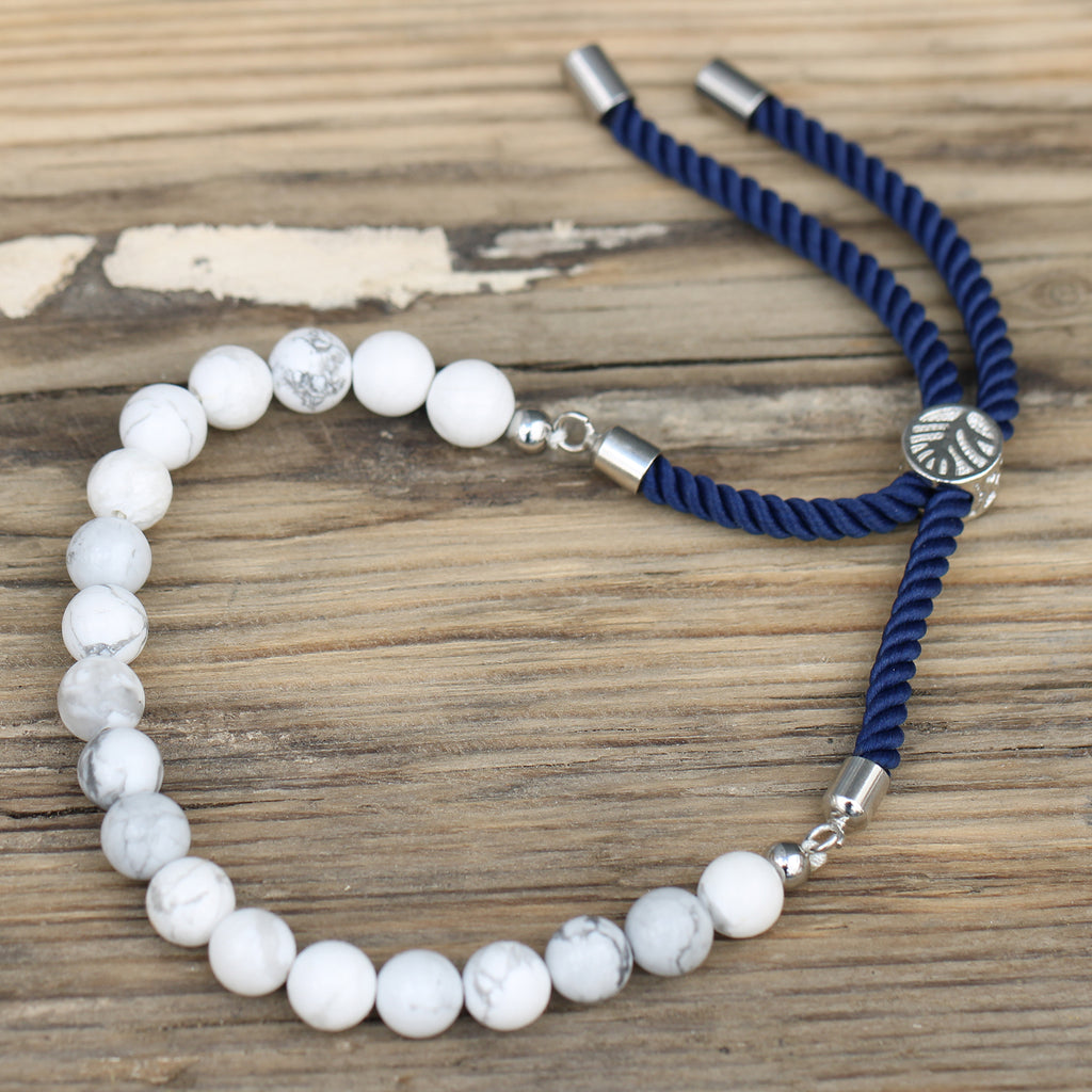 A silver-plated bracelet with navy string detailing and white howlite beads, displayed on a wooden surface.