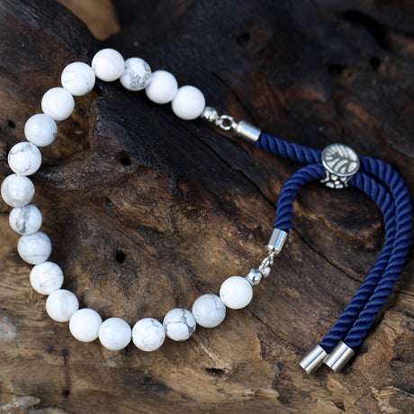 A silver-plated bracelet with navy string detailing and white howlite beads, displayed on a wooden surface.