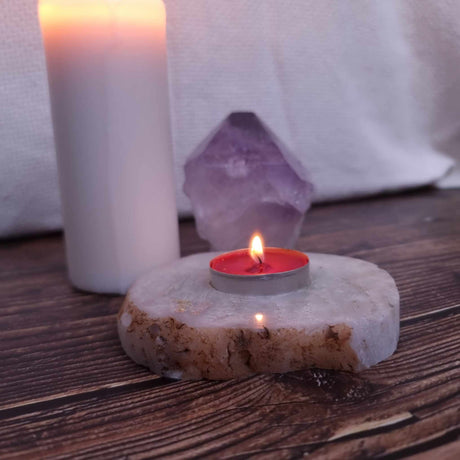 An agate tealight holder with lit red candle on a wooden surface with a pillar candle and crystal in the background