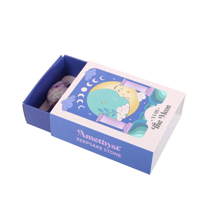 An amethyst crystal moon keepsake stone beside its packaging box, which has 'The Moon' tarot card imagery.