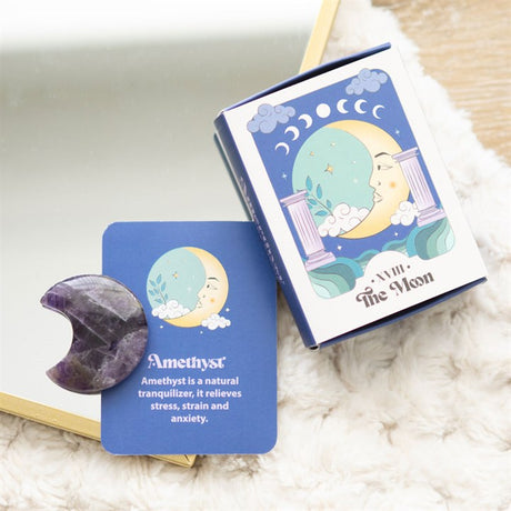 An amethyst crystal moon keepsake stone beside its packaging box, which has 'The Moon' tarot card imagery.