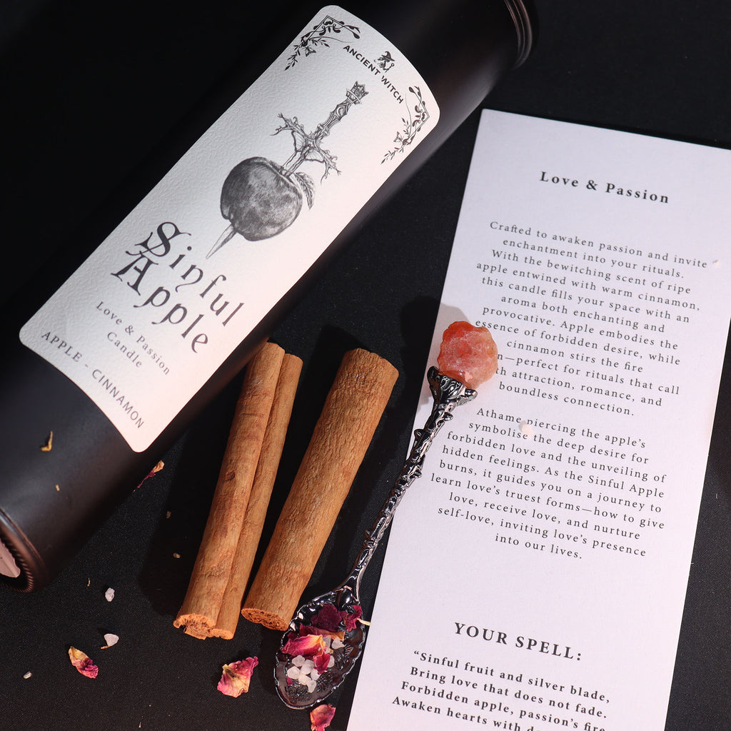 Candle labeled 'Sinful Apple' with cinnamon sticks and a spoon on a dark surface.