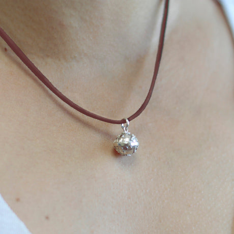 A silver angel bell necklace with a red cord and silver detailing on the necklace and bell.
