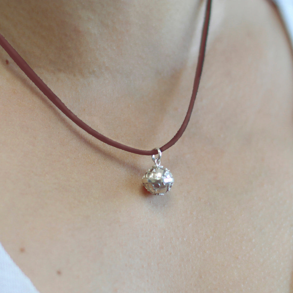 A silver angel bell necklace with a red cord and silver detailing on the necklace and bell.