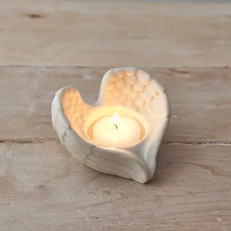 Heart-shaped angel wing candle holder with a lit candle on a wooden surface
