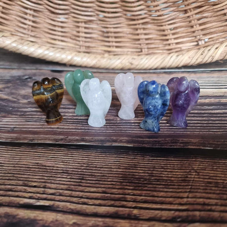 A collection of crystal healing angels in various colours including purple, clear, green, and brown, displayed on a wooden surface.